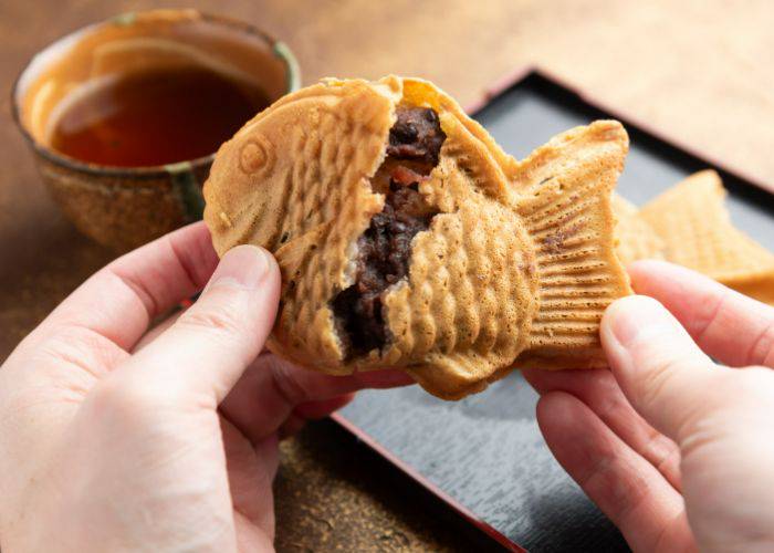 A taiyaki desserts being split open, revealing the red bean paste filling inside.